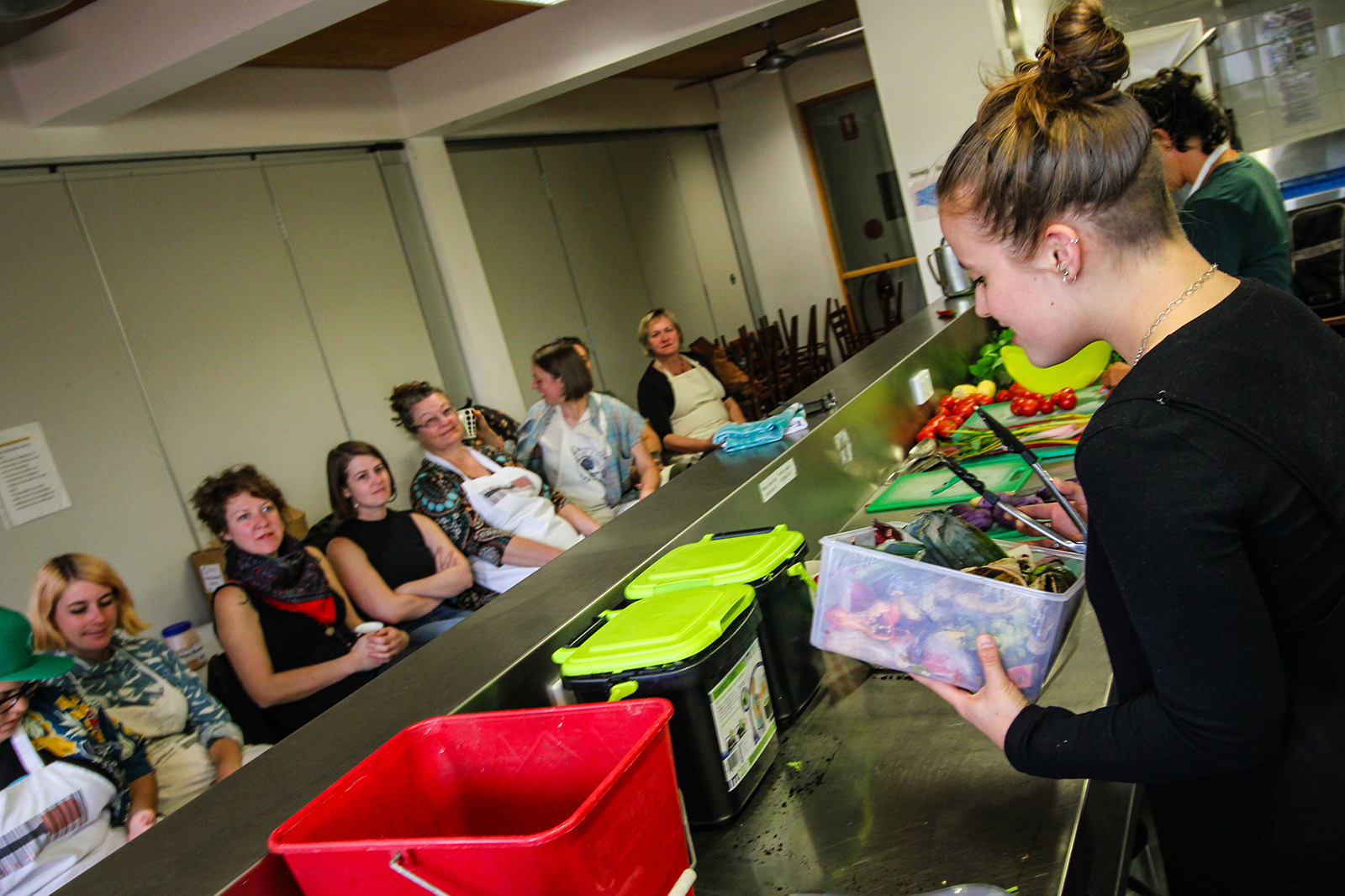 woman with tongs at counter facing seated participants