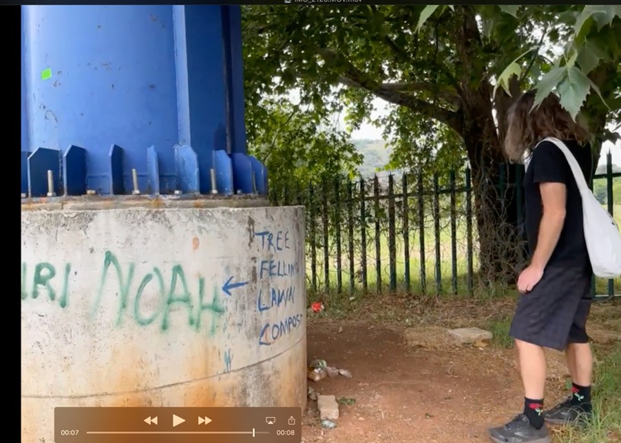Video screenshot of figure walking past a column with a white bag over their shoulder